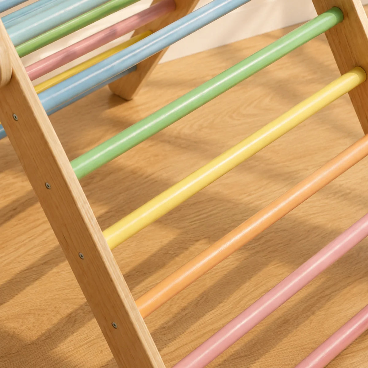 Close-up of a wooden climbing frame with pastel-colored horizontal bars in green, yellow, peach, pink, blue, and light green on a light wood floor.