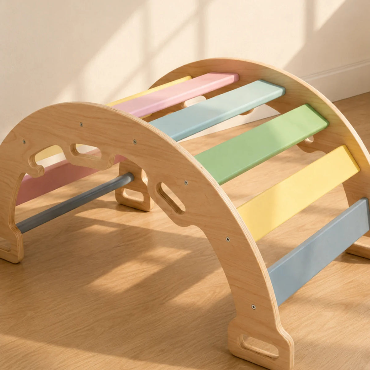 A wooden arched climbing or play structure with pastel-colored slats in pink, yellow, green, blue, and gray, photographed indoors on a wood floor against a light wall.