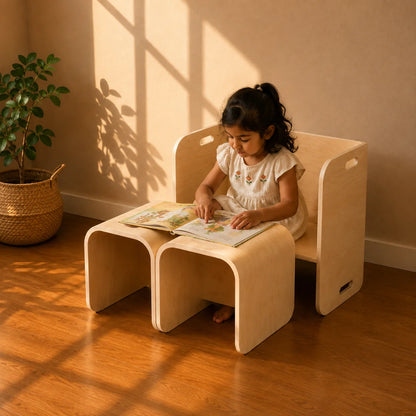 A young girl sits on a light natural wood children's chair with integrated side tables, reading a book in a sunlit room with warm sunlight and shadows on the wall and floor.