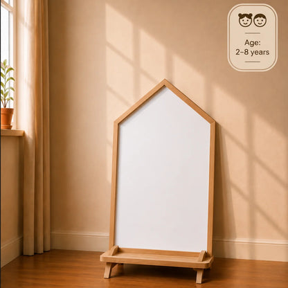 A house-shaped wooden easel with a white writing board, set against a warm beige wall with window shadows. A small age rating badge in the top right reads 'Age: 2-8 years'.