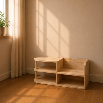 A light natural wood two-tier storage shelf with curved sides, placed in a minimalist room corner with beige walls, warm sunlight streaming in, and a small potted plant on a windowsill.