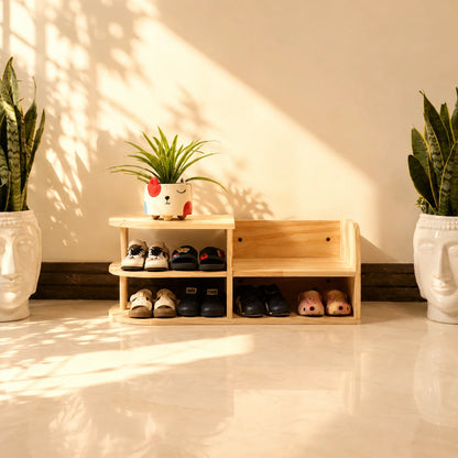 A light natural wood shoe rack with open shelves and a small planter on top, styled in a warm, sunlit entryway with potted snake plants on either side.