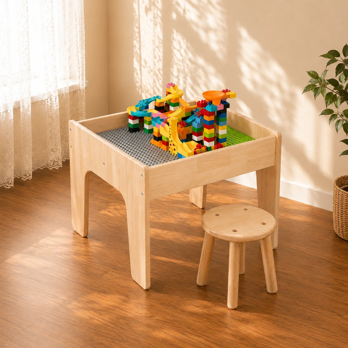 A light natural wood children's play table with a built-in gray pegboard and a matching wooden stool, shown in a sunlit room with a plant and curtains in the background.