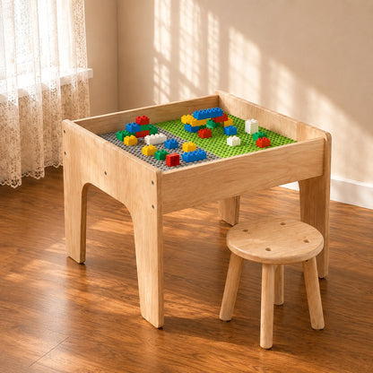 A light natural wood children's activity table with a built-in play grid, shown with colorful toy blocks on top and a matching small wooden stool in a sunlit room.
