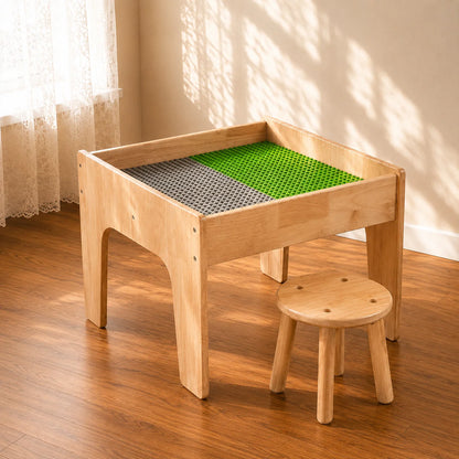 A light natural wood children's activity table with a green and gray textured play mat inside, shown with a matching small wooden stool in a sunlit room with a wood floor and cream walls.