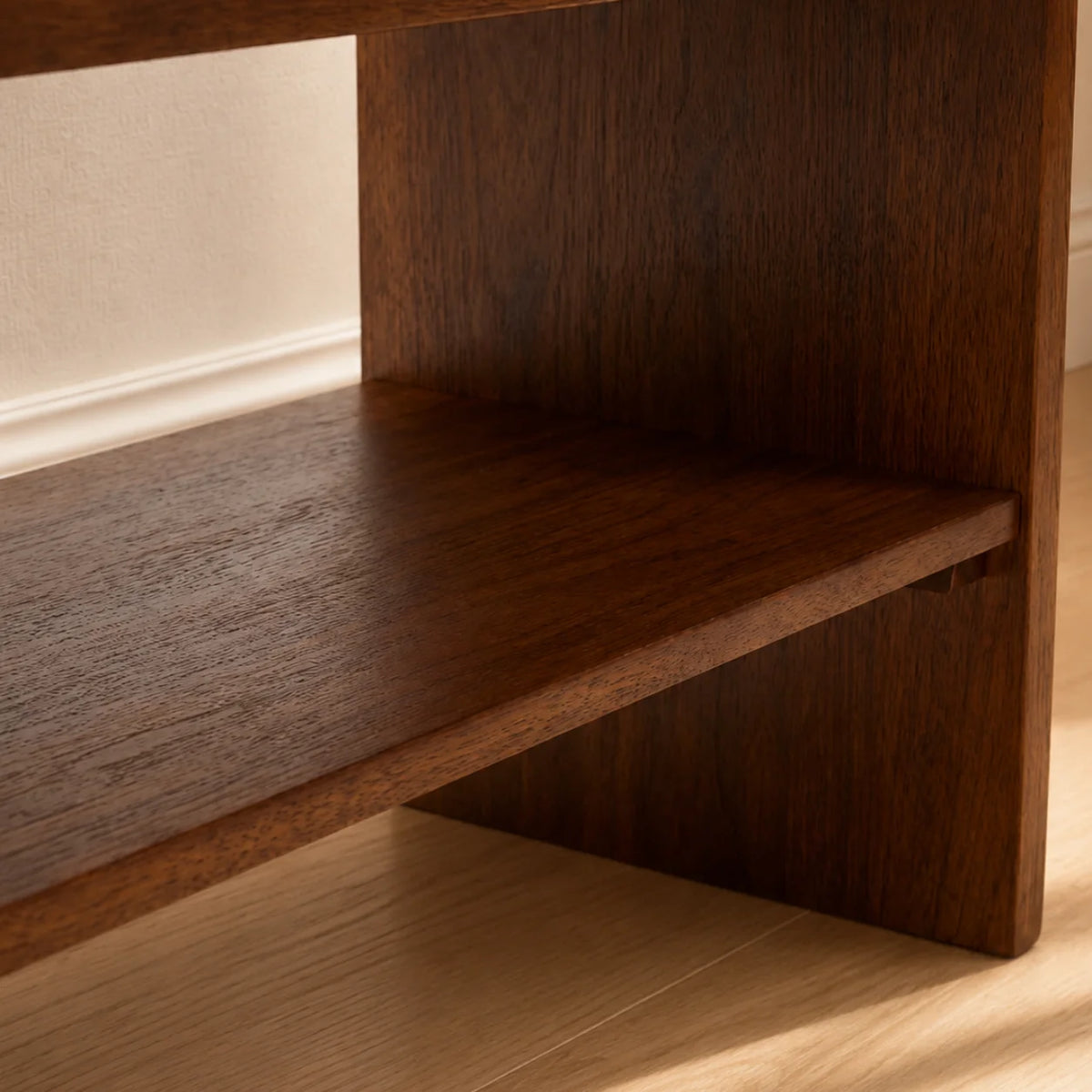Close-up of a dark brown wooden shelf with a visible wood grain texture, set against a light beige wall and light wood floor.