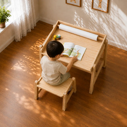 A light natural wood children's desk with a matching stool in a sunlit room with hardwood floors, sheer curtains, and framed animal artwork on the wall.